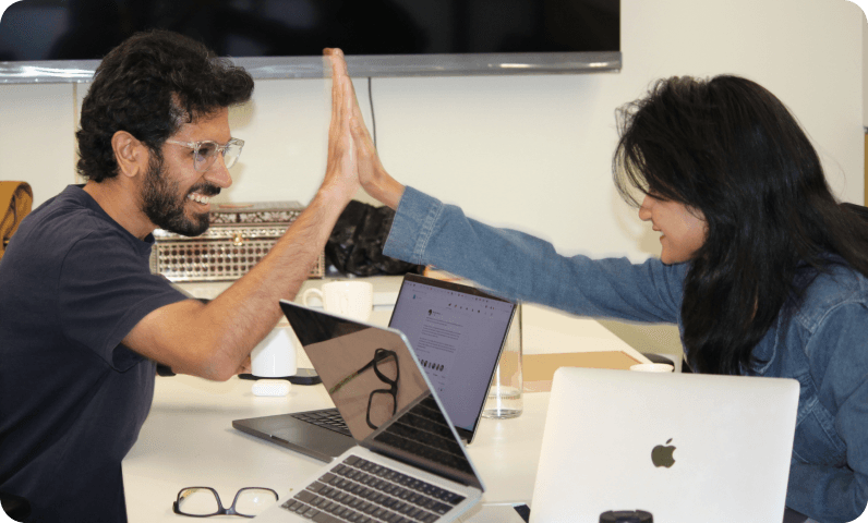 Two teammates high-fiving across laptops at a desk